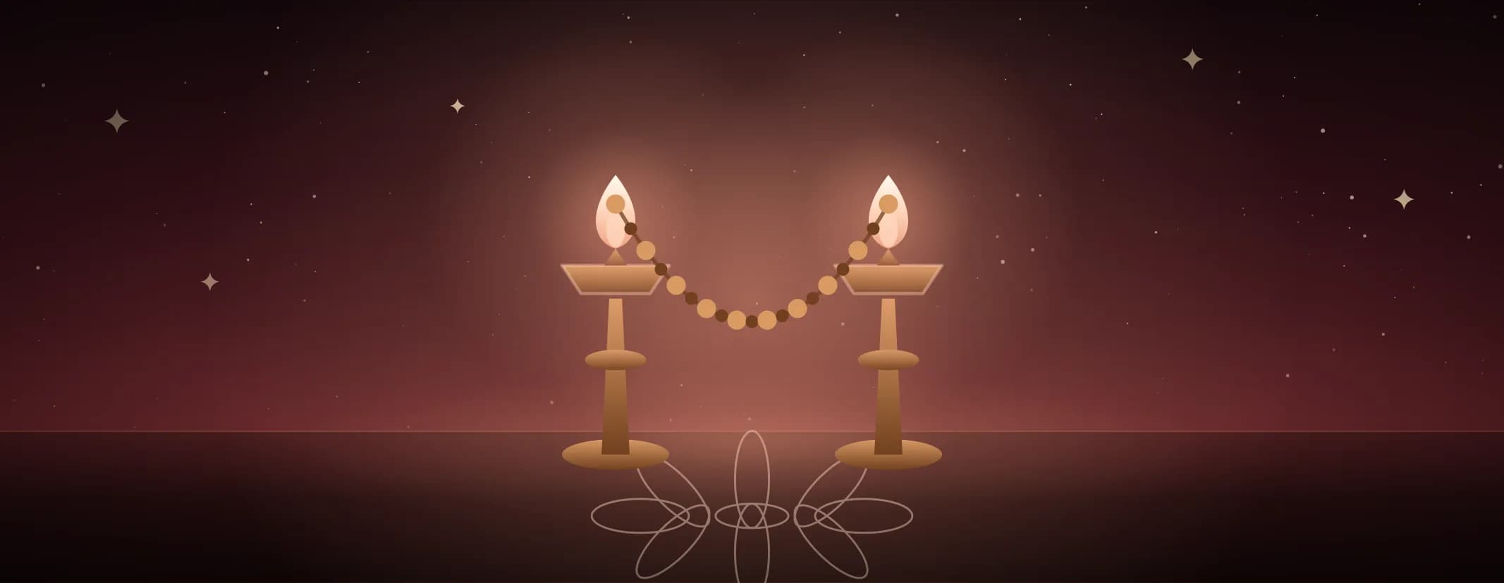 Two brass lamps both lit, a beaded garland slung in a curve between them over a kolam floor, in warm red light, the subject set well to the left of the frame.