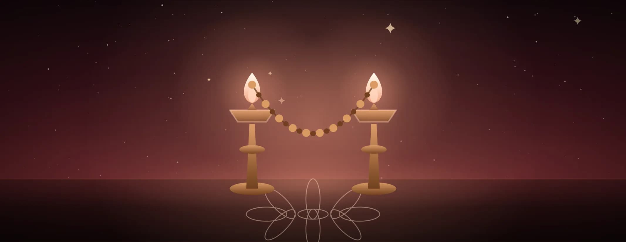 Two brass lamps facing each other, both lit, joined by a beaded garland, on a kolam floor in warm red light.