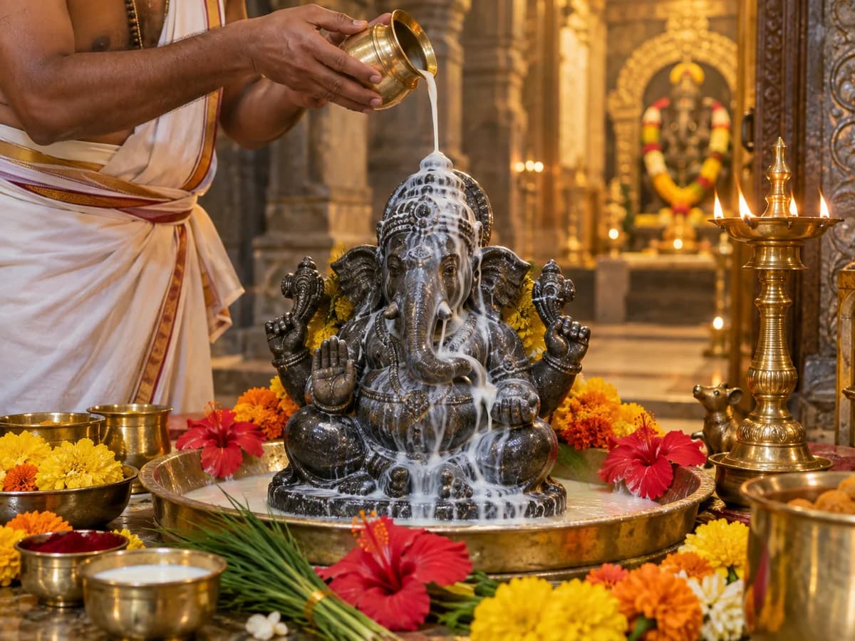 A Purohit pours milk over a stone Ganapathi idol during abhishekam.
