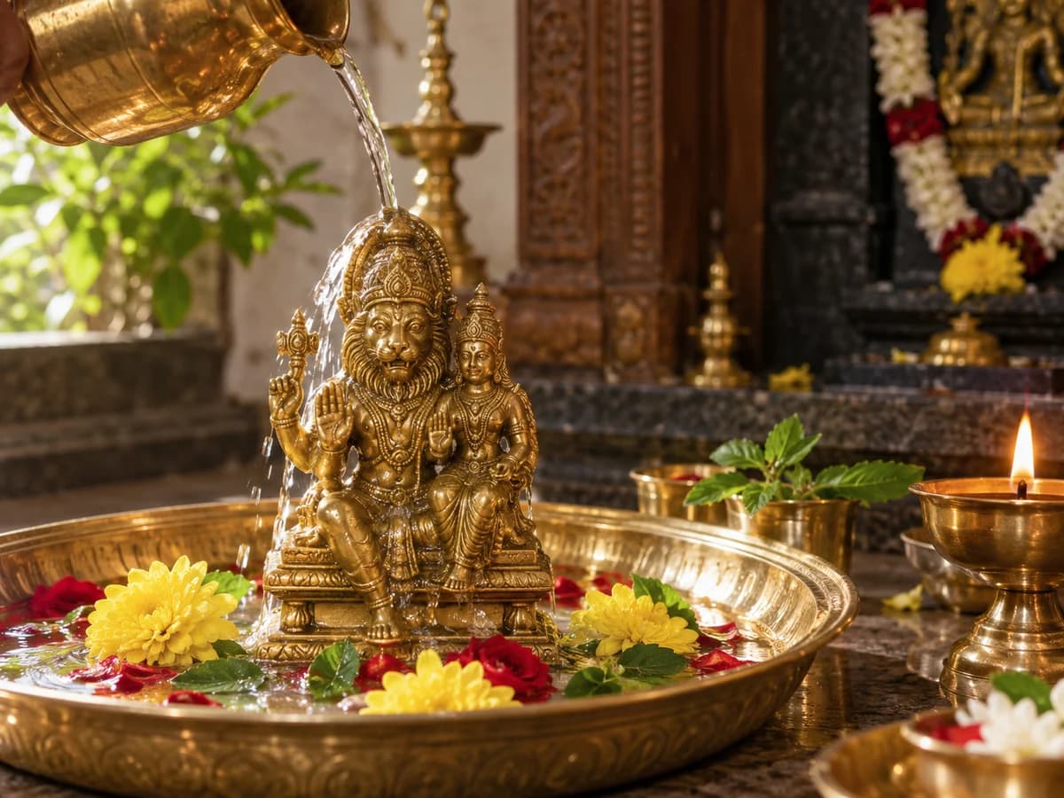 Water offered over a seated Lakshmi Narasimha idol surrounded by flowers and a lamp.