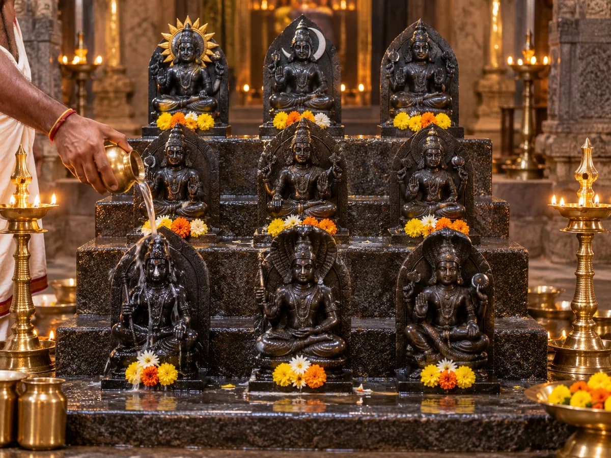 Water is poured over a Navagraha idol among nine stone deities on a temple pedestal.